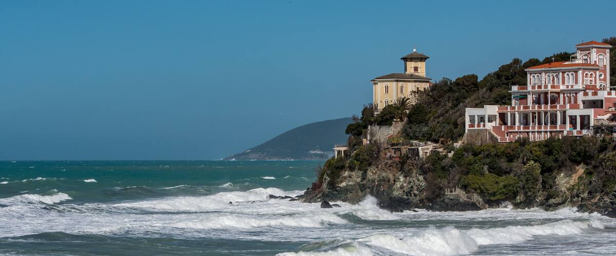 A coastal town with a lighthouse and buildings on a cliff overlooking the ocean.