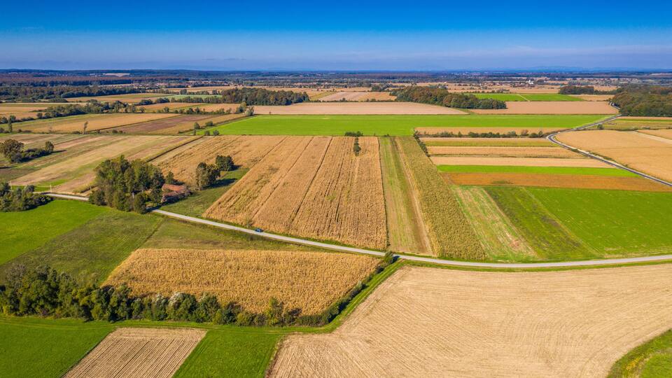 An aerial view of a rural landscape with fields, a winding road, and distant hills.