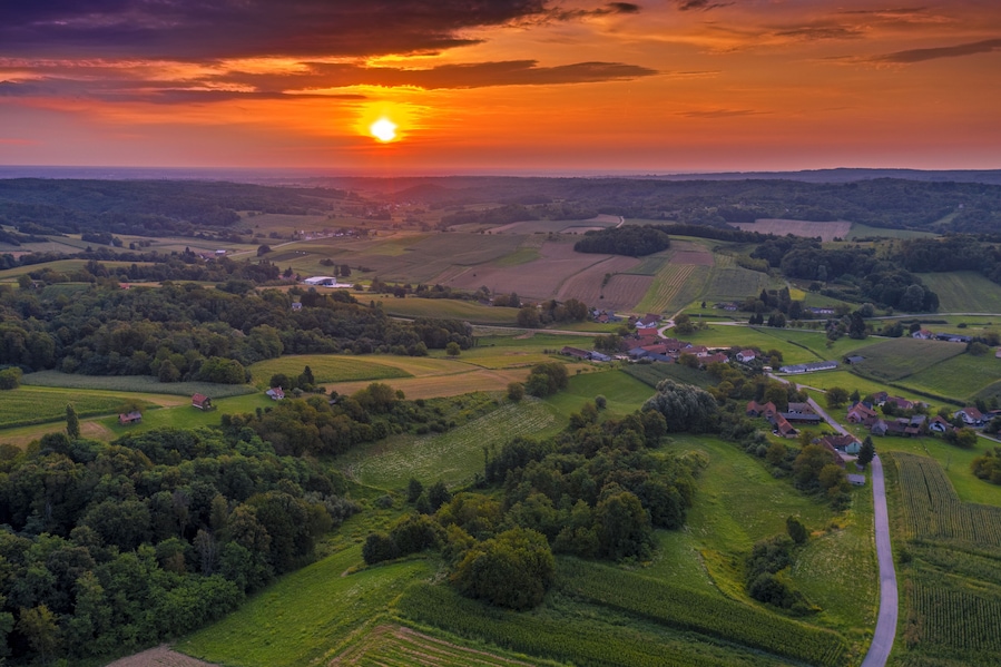 Paisaje rural con colinas ondulantes, campos y casas dispersas al atardecer.