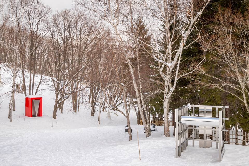 Un paisaje nevado con una estructura roja y un banco blanco.