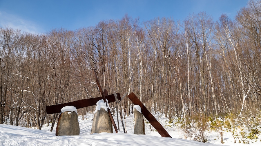 A snow-covered landscape with a metal sculpture of a tilted structure amidst trees.