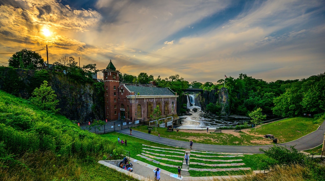 A historic building with a waterfall, a paved area with steps, and lush greenery.