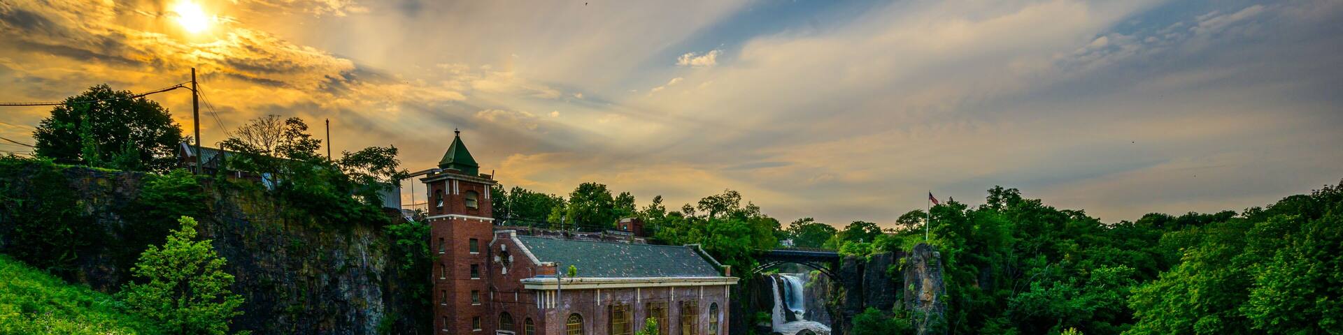 A historic building with a waterfall, a paved area with steps, and lush greenery.