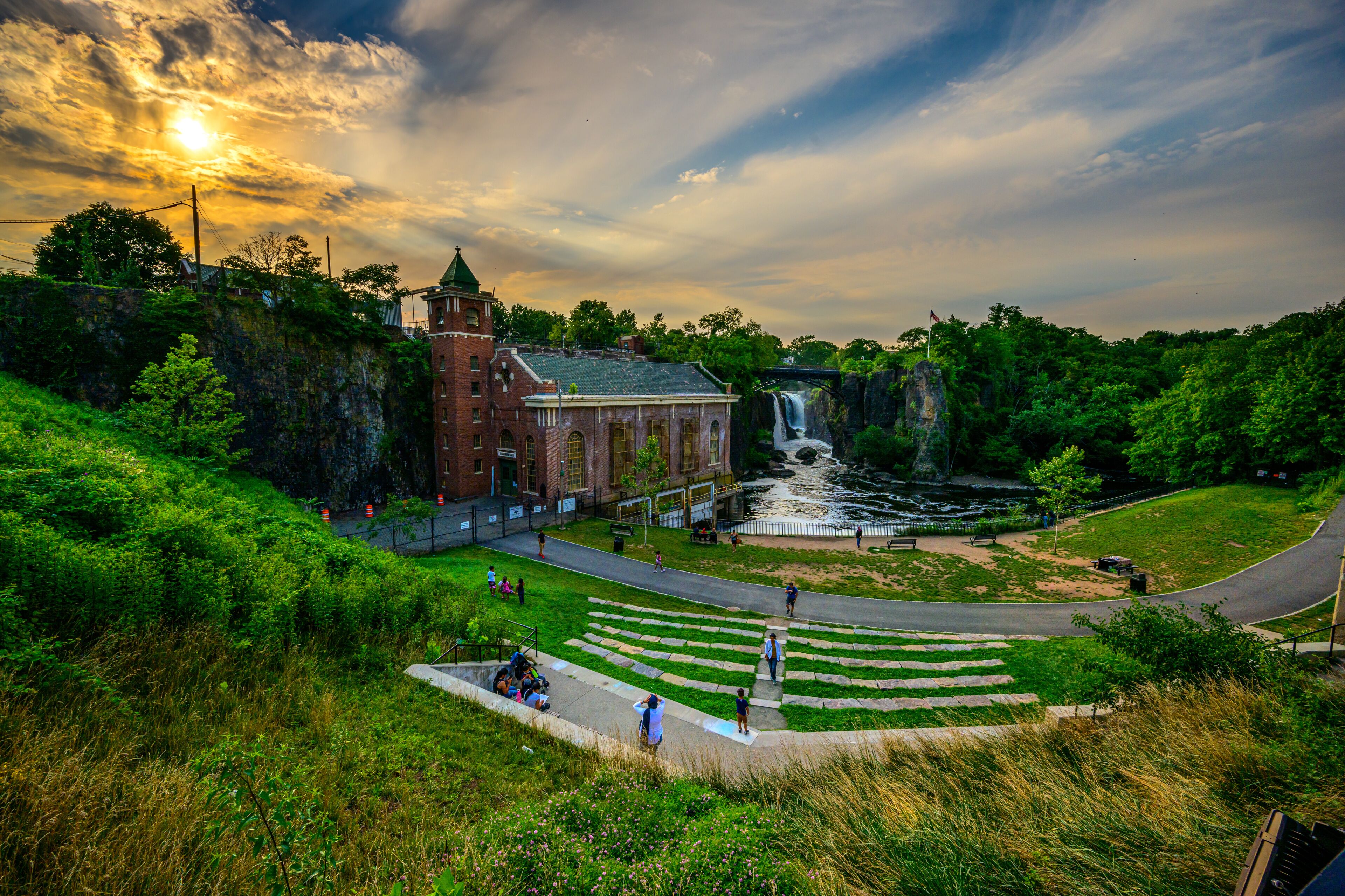 A historic building with a waterfall, a paved area with steps, and lush greenery.
