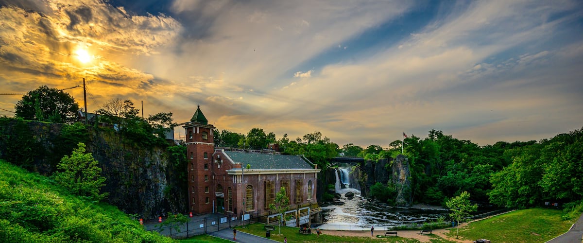 A historic building with a waterfall, a paved area with steps, and lush greenery.