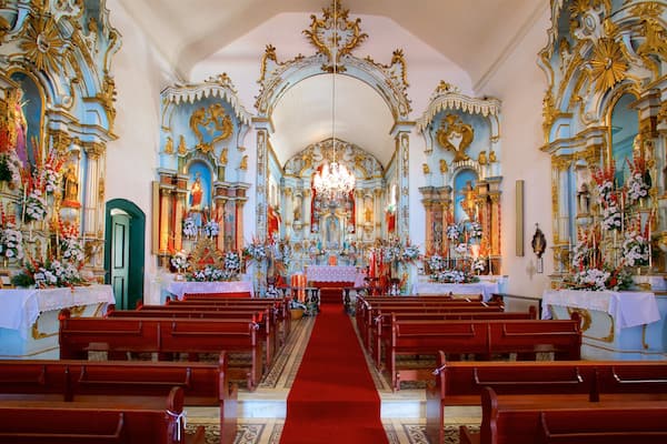Ein kunstvoll gestalteter Kircheninnenraum mit roten Kirchenbänken, einem zentralen Altar und aufwendigen goldenen und blauen Verzierungen.