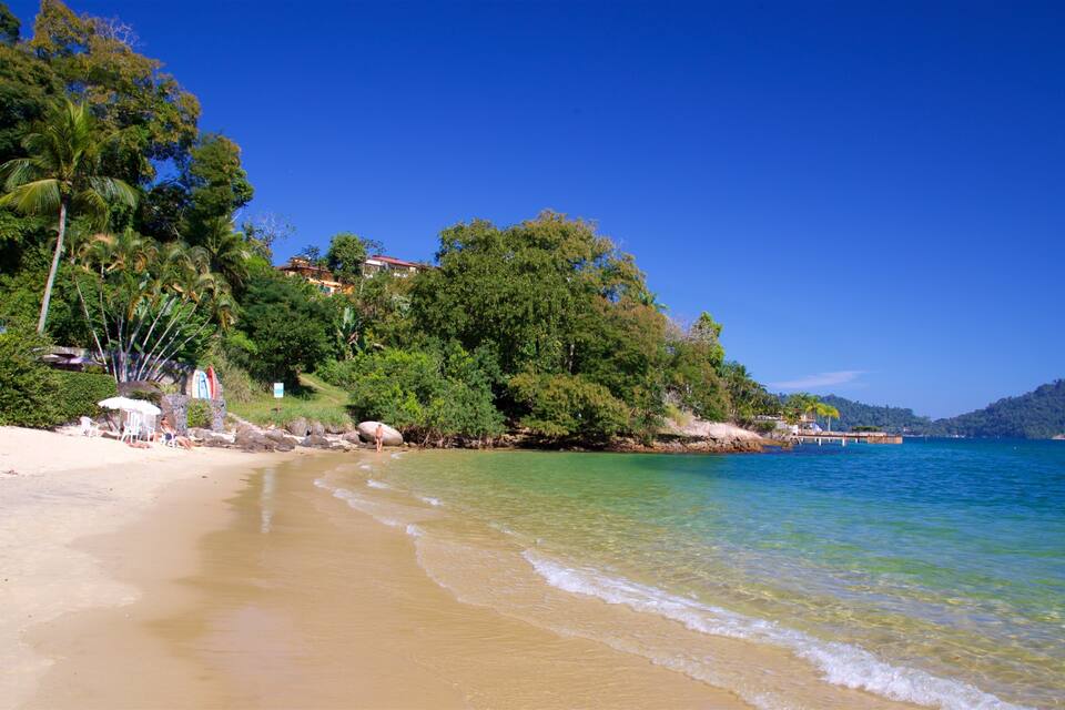 Uma praia com águas turquesa cristalinas, areal arenoso e árvores verdejantes.