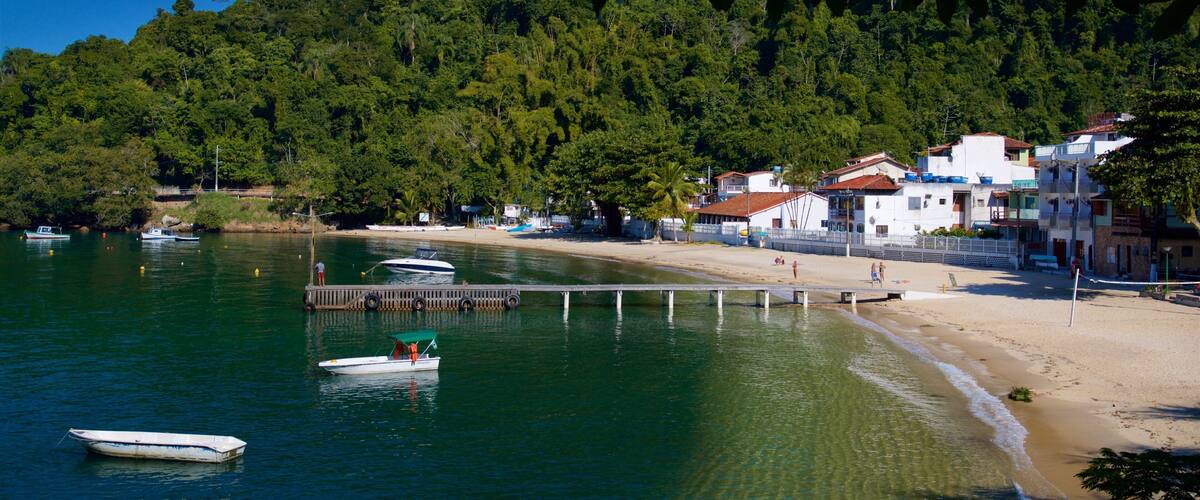 A coastal village with boats on calm waters, a sandy beach, and dense forested hills.