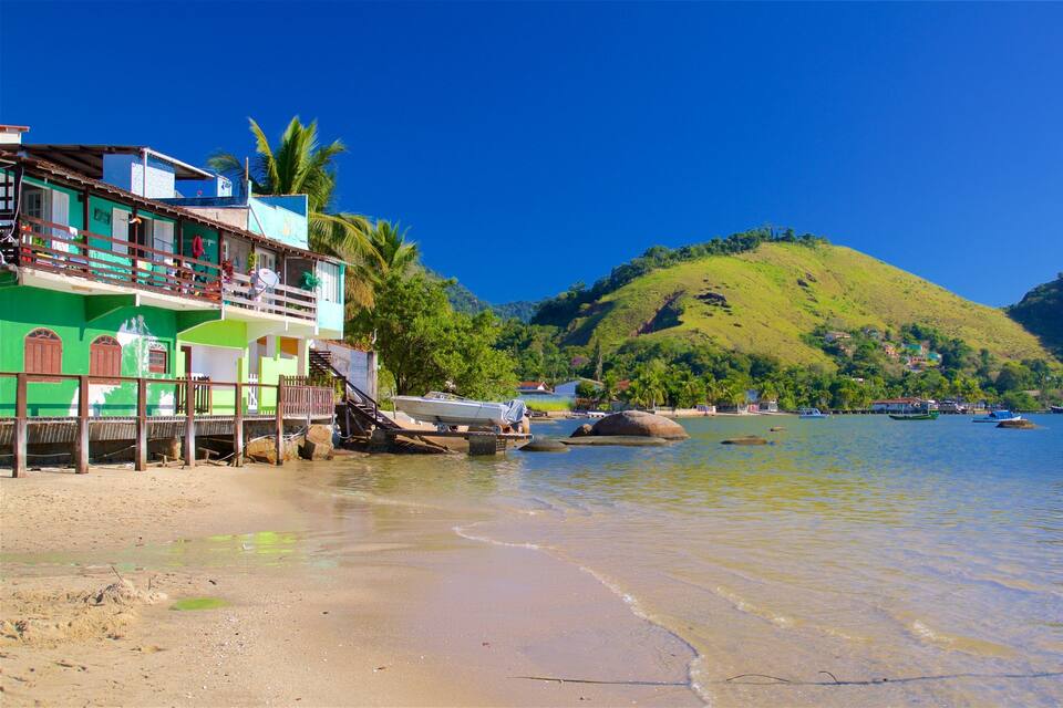 Uma praia com barcos, um edifício verde e uma colina ao fundo.