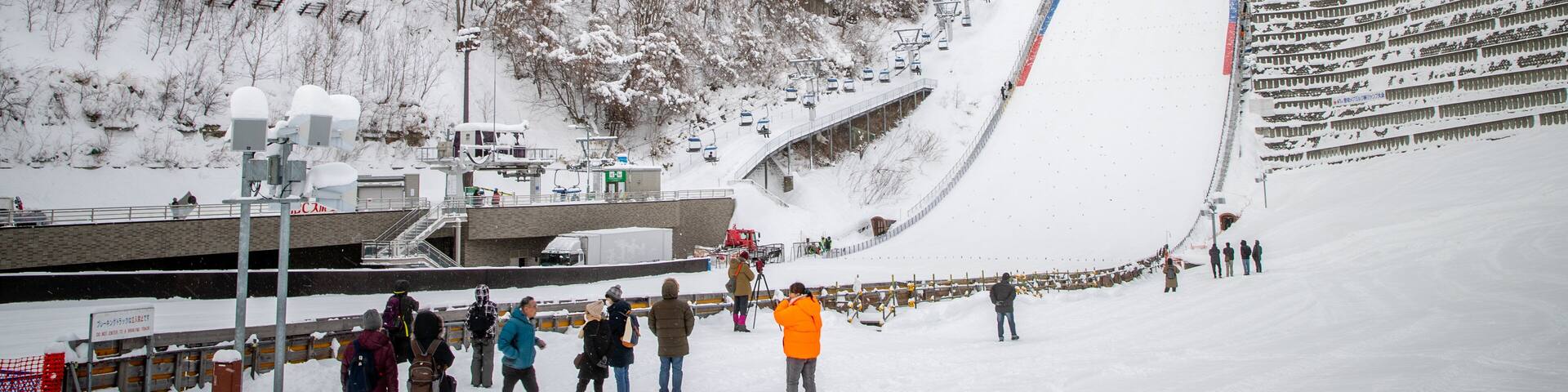 A snowy ski slope with a ski lift, a ski area, and a forested hillside.