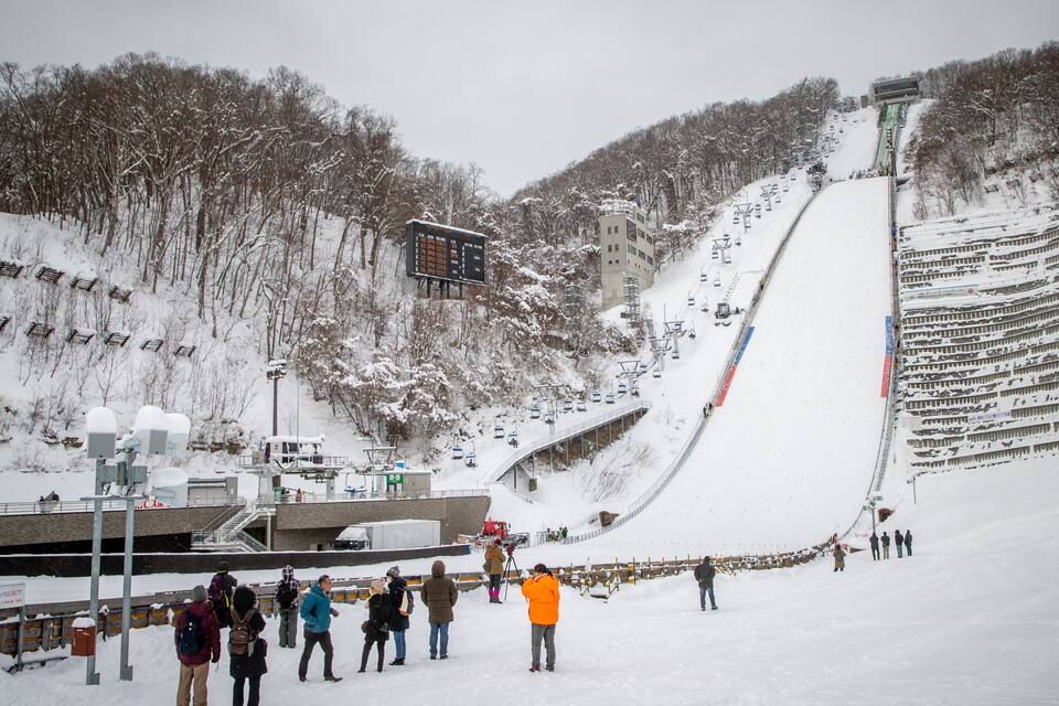 A snowy ski slope with a ski lift, a ski area, and a forested hillside.