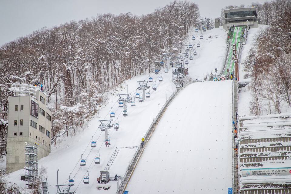 Una pista d'esquí nevada amb un teleàs, arbres i un edifici.