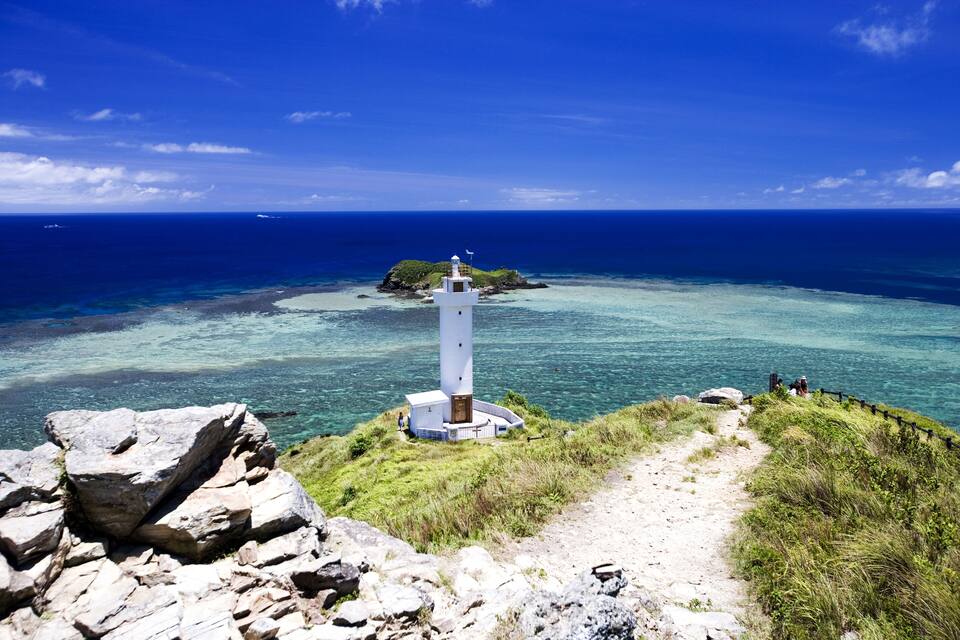 A lighthouse on a rocky outcrop with clear blue waters and a distant island.