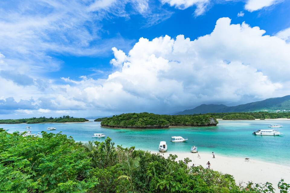 A tropical island with clear turquoise waters, boats, and lush greenery.