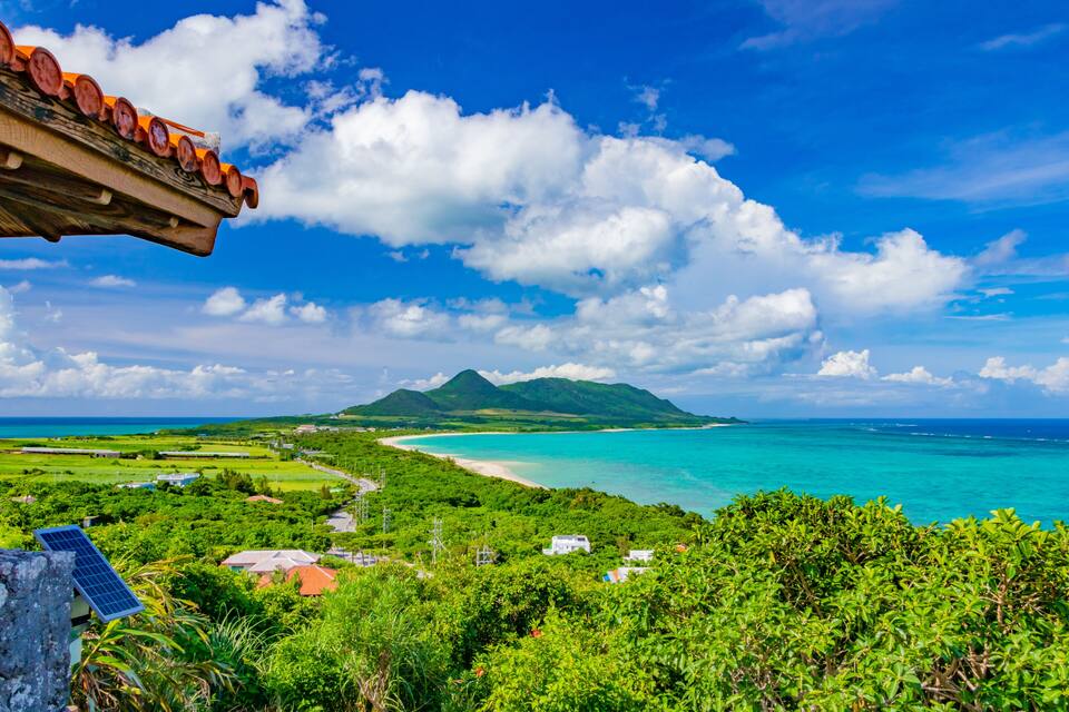 A coastal landscape with a mountain, turquoise waters, and lush greenery.
