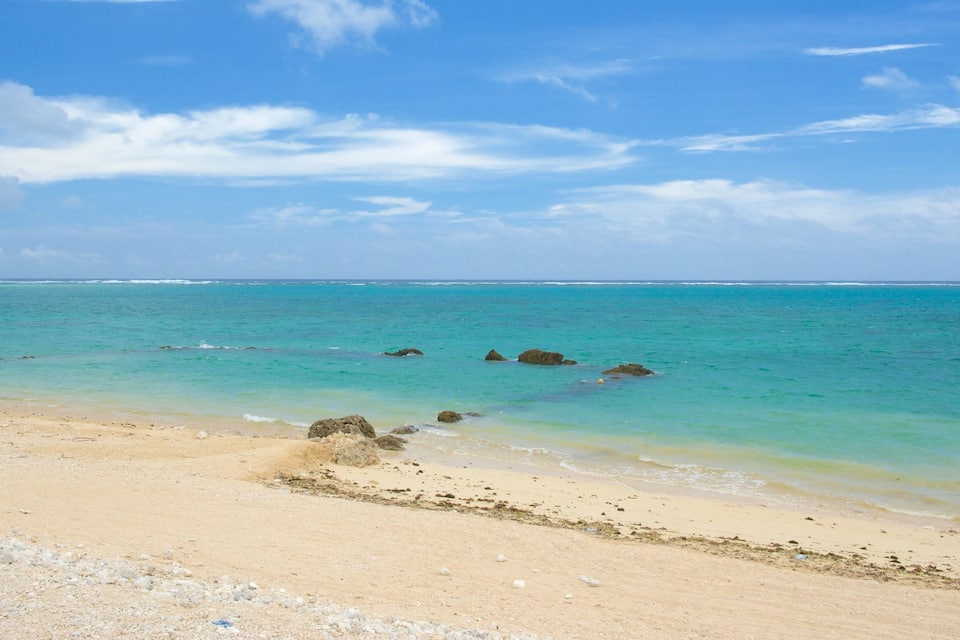 Una platja sorrenca amb aigua turquesa cristal·lina i roques disperses.