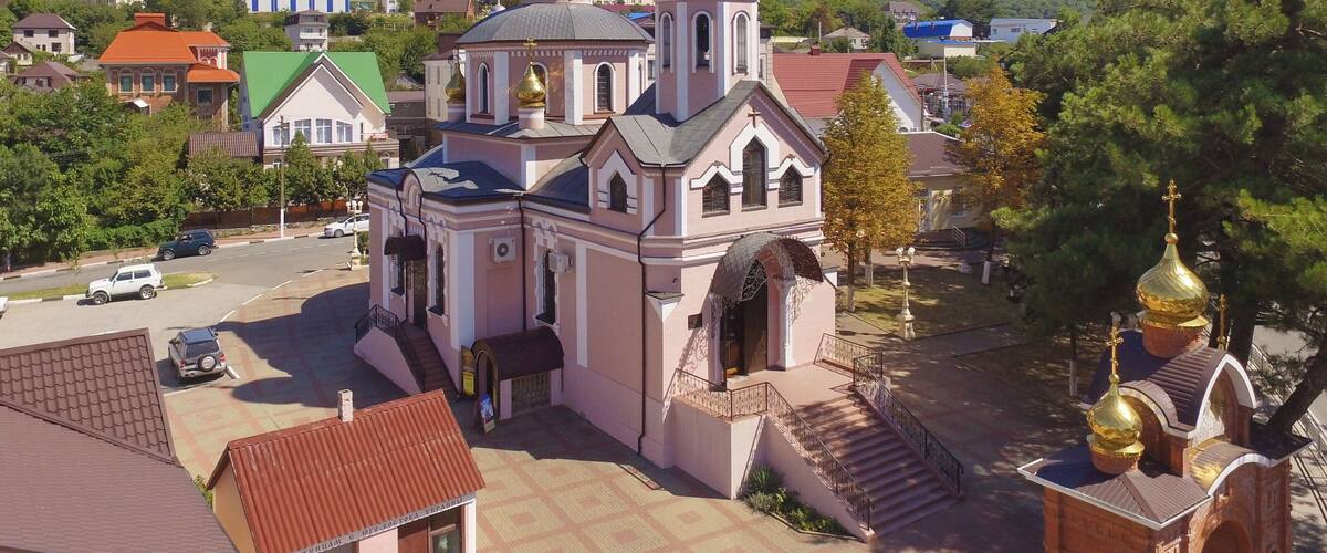 A church with golden domes and a bell tower, surrounded by residential buildings and trees.
