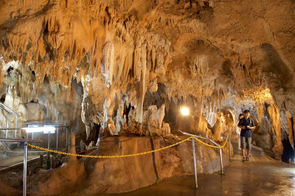 Cueva con estalactitas y estalagmitas, baranda de metal y una barrera de cuerda amarilla.