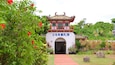 A traditional Chinese gate with a red roof and white walls, surrounded by lush greenery and red flowers.
