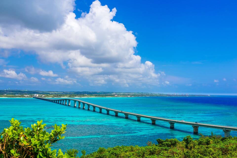 A long bridge over turquoise waters with a clear sky and greenery in the foreground.
