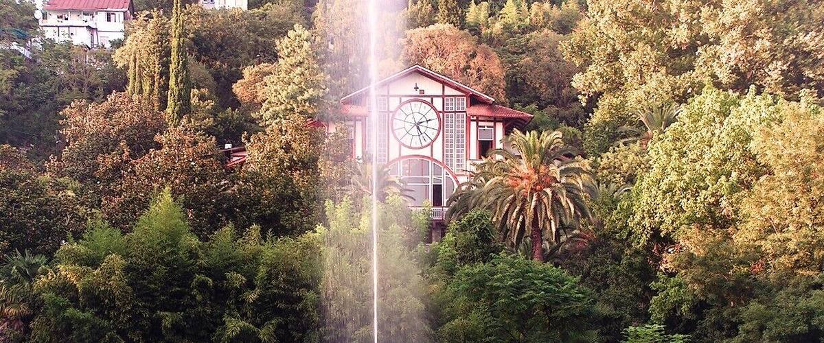 A fountain with a statue in a park with trees and a building in the background.