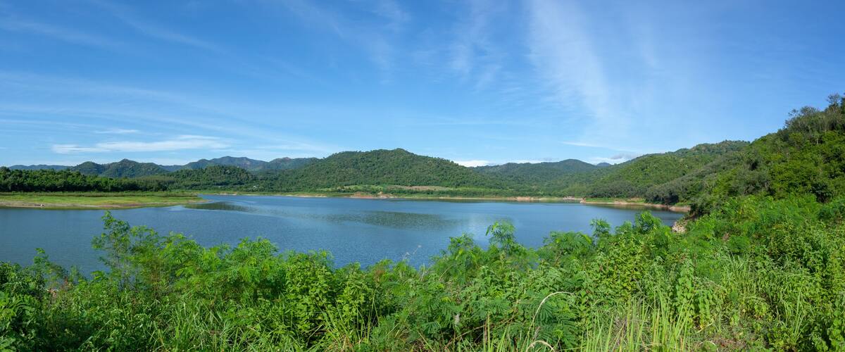 A lake surrounded by lush greenery and distant mountains under a clear blue sky.