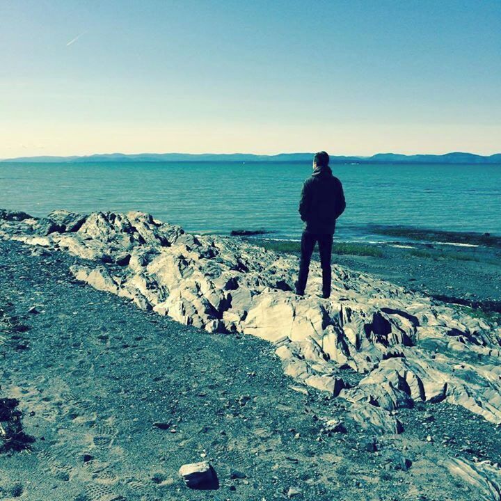 A person standing on rocky terrain by a body of water with distant mountains.