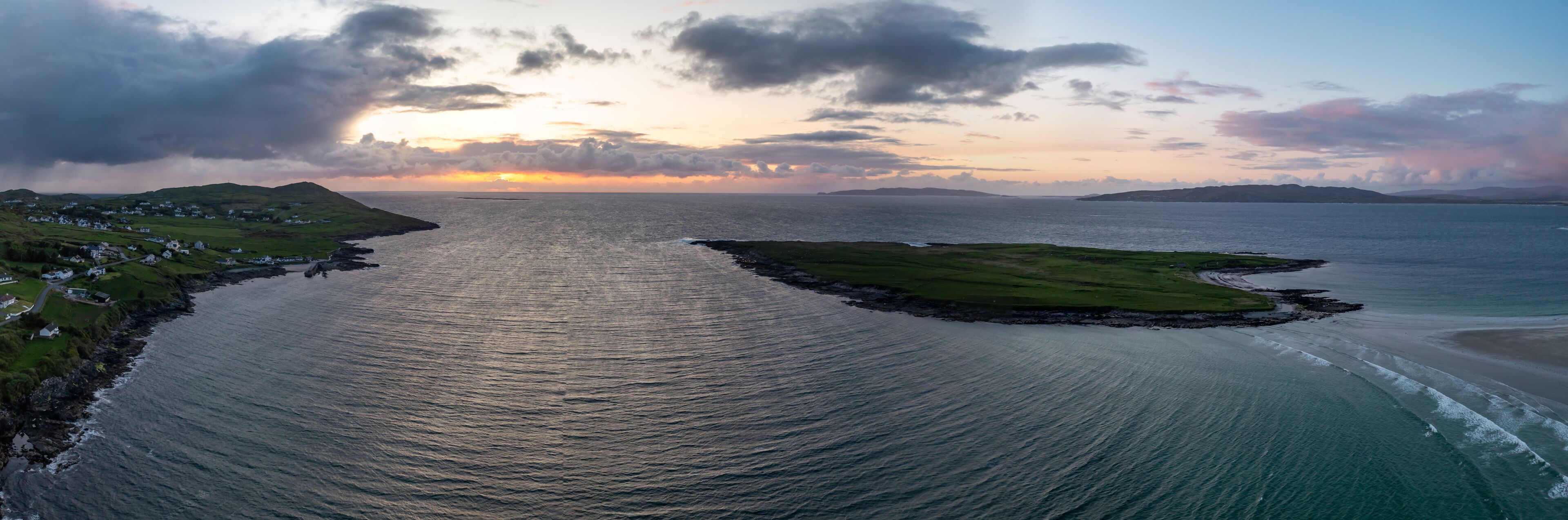 A coastal landscape with a narrow waterway, grassy areas, and a distant shoreline.