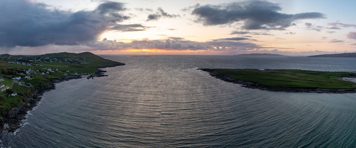 A coastal landscape with a narrow waterway, grassy areas, and a distant shoreline.