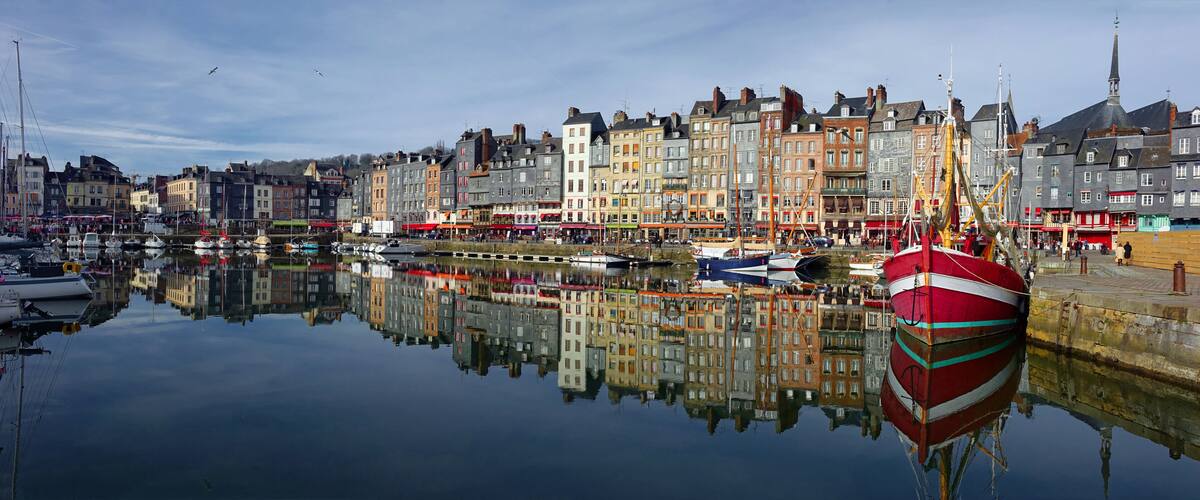 A harbor with boats, a red and white striped boat, and colorful buildings reflecting in the water.