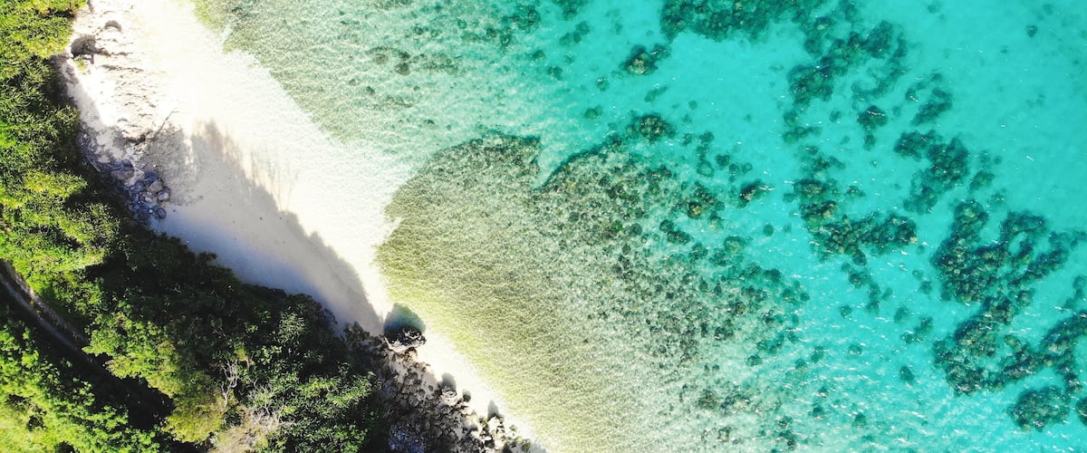 A turquoise beach with white sand and clear water, surrounded by lush greenery.