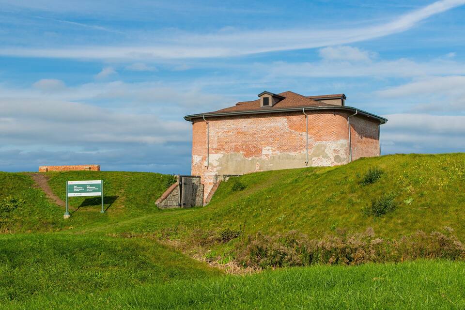 Un edifici de maó damunt d'una collada verda sota un cel serè.