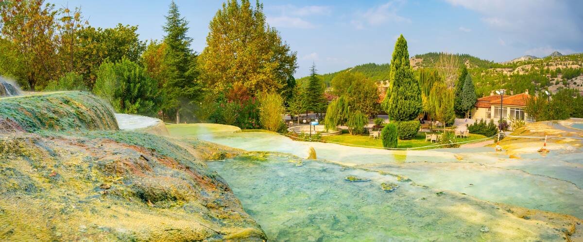 A geothermal area with mineral pools, trees, and a building in the background.