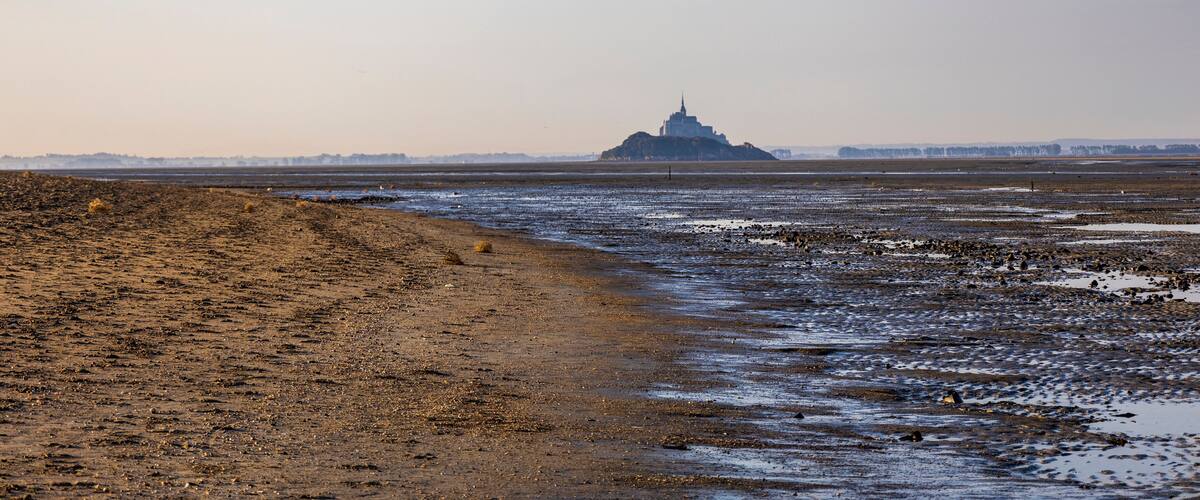A coastal landscape with a sandy beach and a distant hill with a structure.