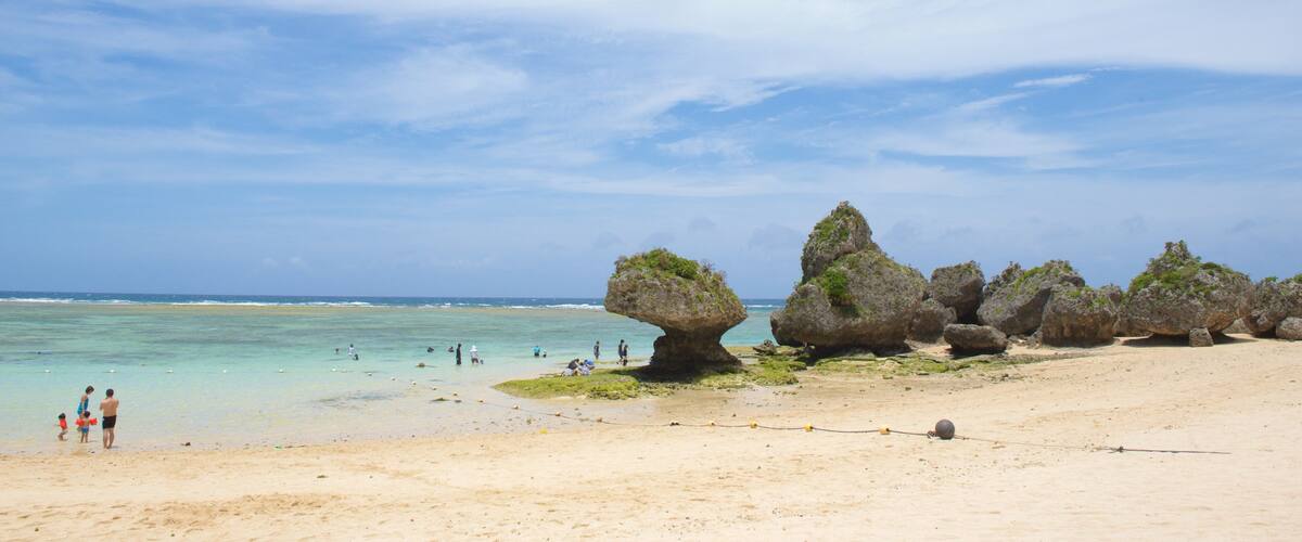 A beach with clear turquoise waters, a sandy shore, and distinctive rock formations with green vegetation.