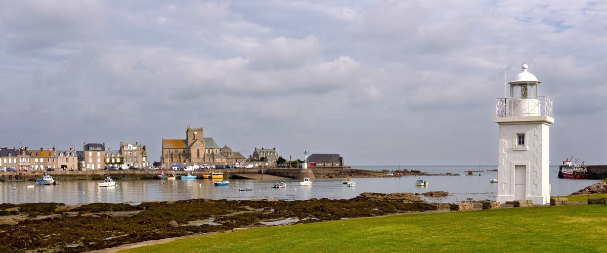 A coastal town with a prominent white lighthouse, historic buildings, and boats on the water.