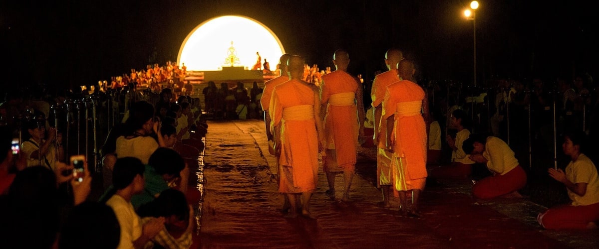 Monks walking down a street at night with a large illuminated structure in the background.