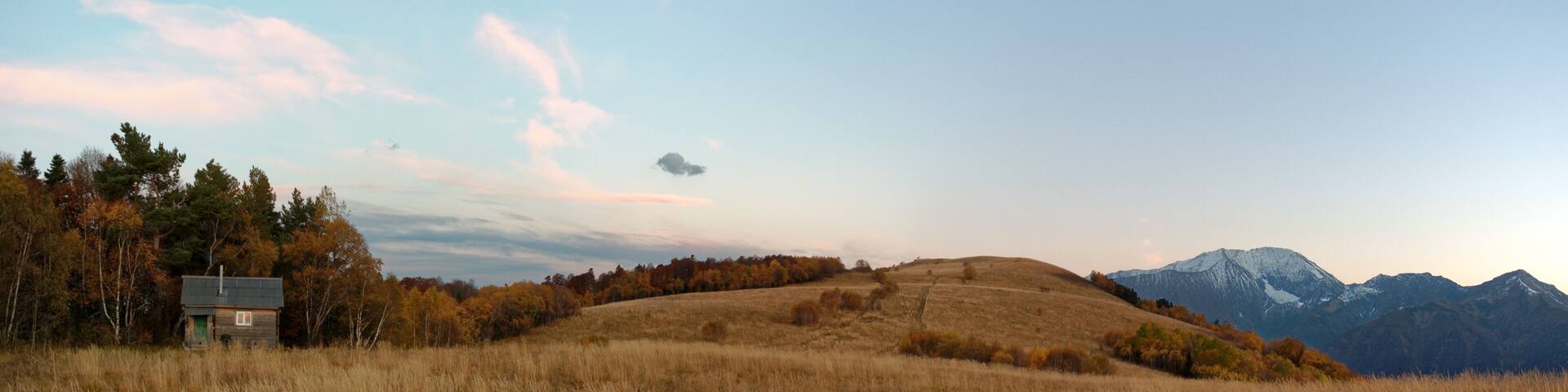 Autumnal subalpine landscape at sunset with snowy mountain peaks, forest, and meadow. Caucasus. Russia. The Caucasian reserve. Pasture Abago