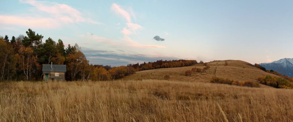 A grassy field with a small cabin and a mountain range in the background.
