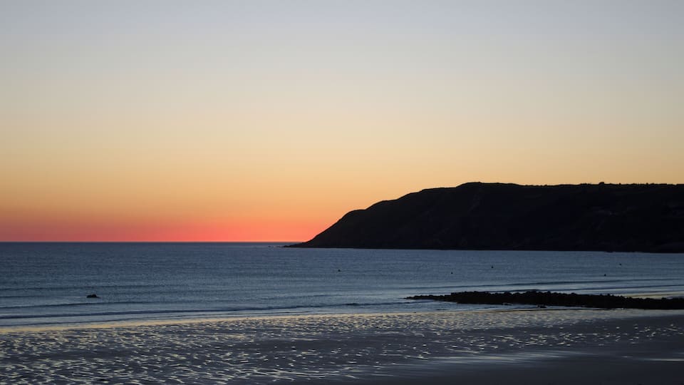 A sunset over a beach with calm waters and a rocky cliff.