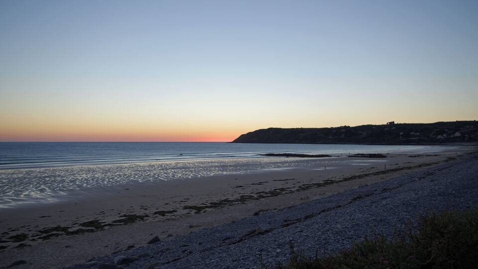 A beach with pebbles and a calm sea at sunset.