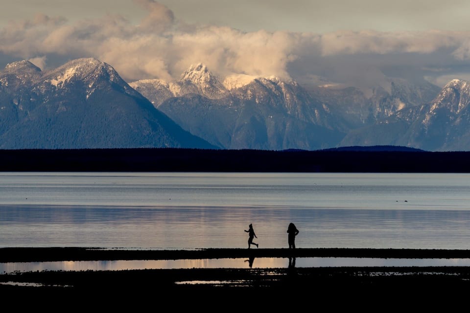A mountain range with snow-capped peaks and a calm lake in the foreground.
