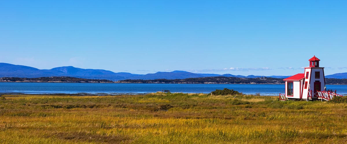 A lighthouse by a lake with mountains in the background.