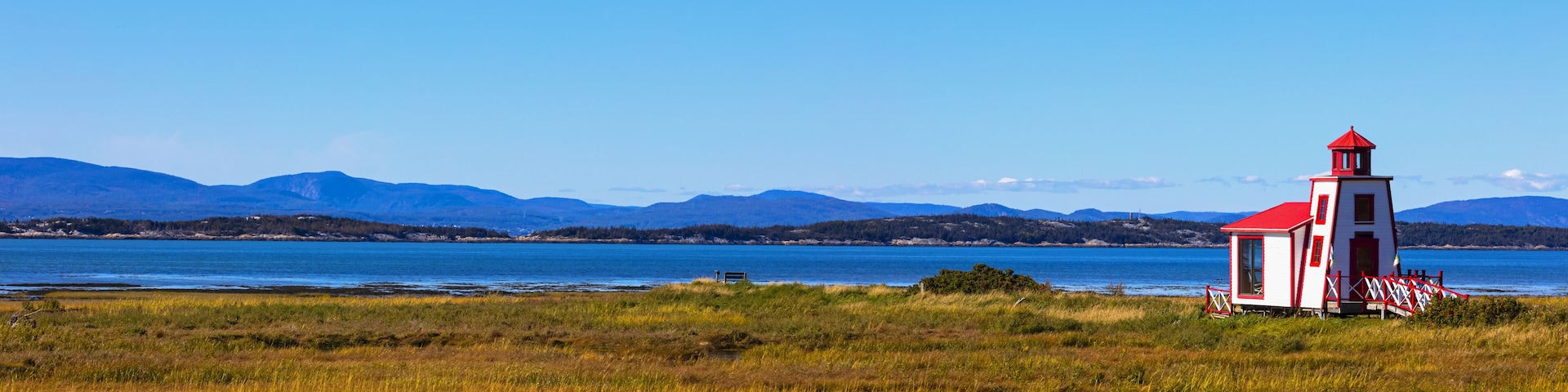 A lighthouse by a lake with mountains in the background.