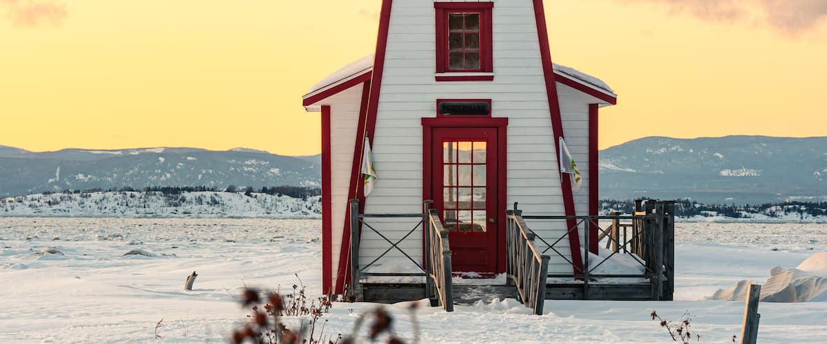 A red and white lighthouse in a snowy landscape with mountains in the background.
