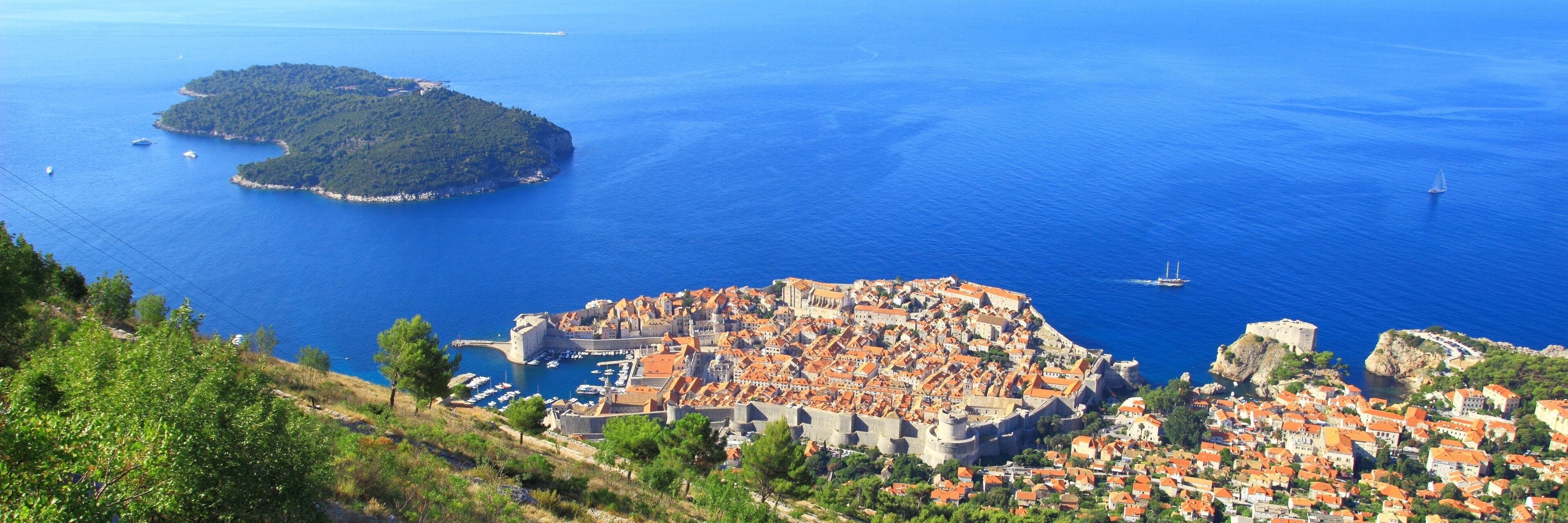 A coastal town with a historic fortification, a small island, and a clear blue sea.
