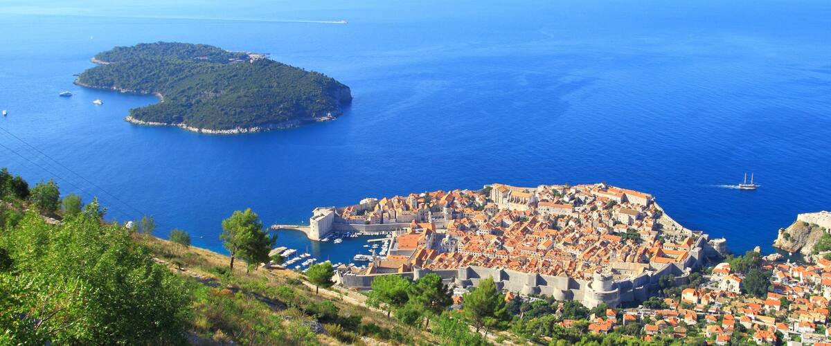 A coastal town with a historic fortification, a small island, and a clear blue sea.