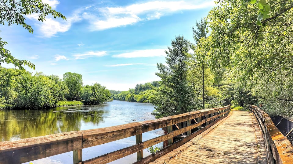 A wooden boardwalk along a river surrounded by lush greenery.