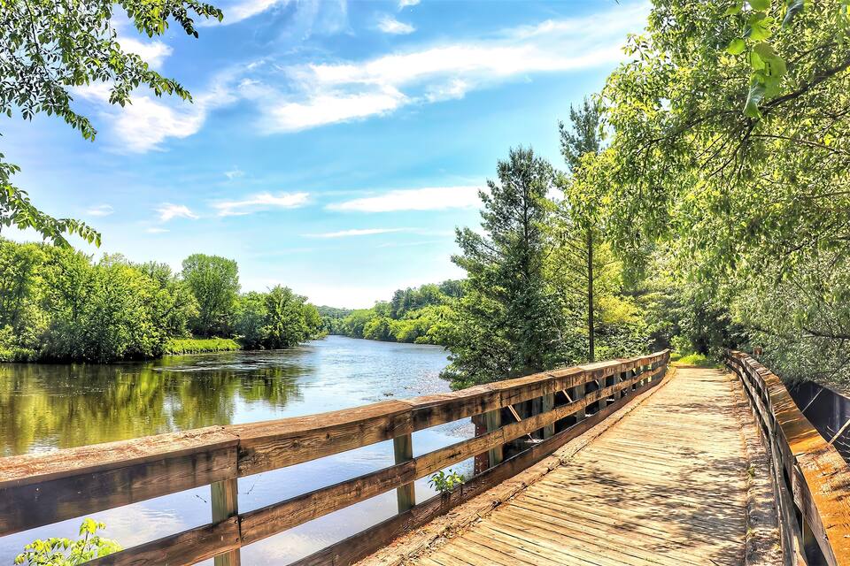 A wooden boardwalk along a river surrounded by lush greenery.