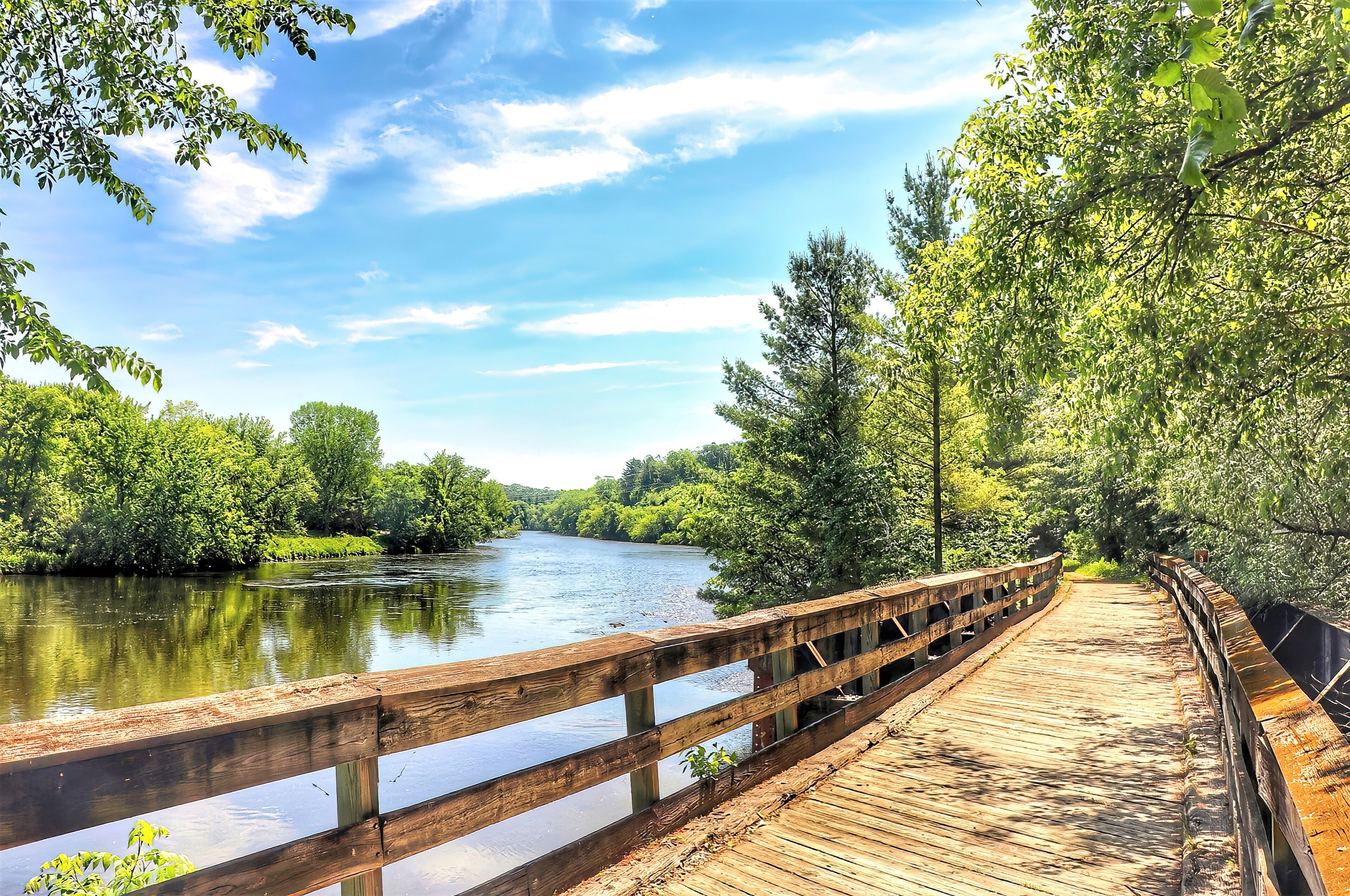 A wooden boardwalk along a river surrounded by lush greenery.